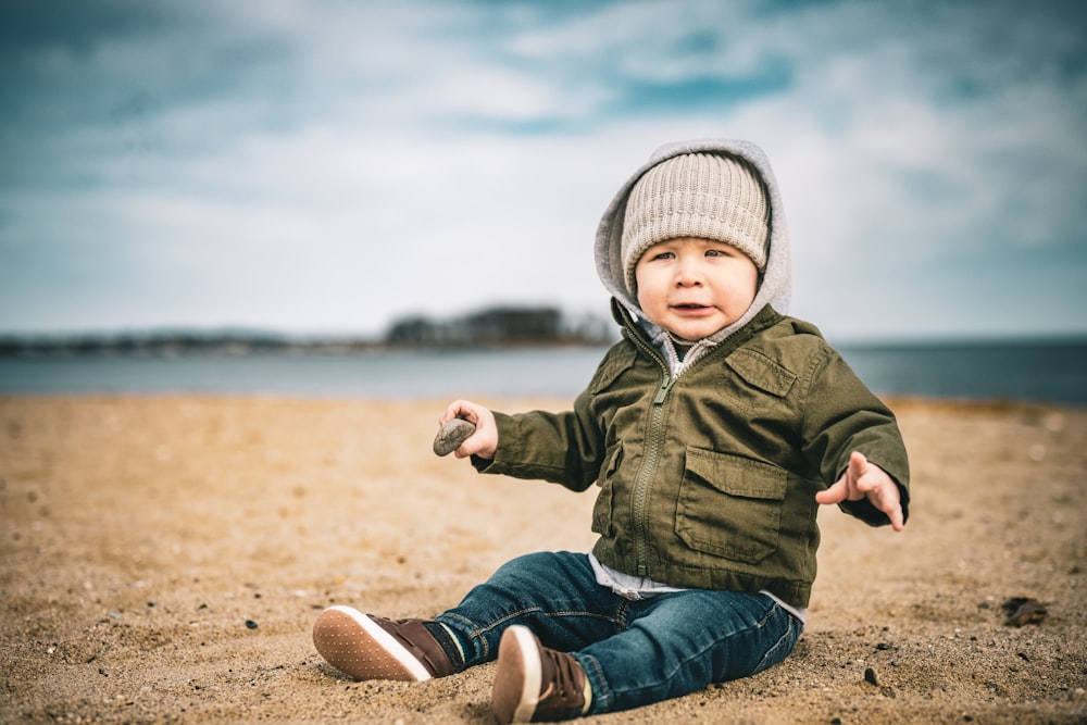 a little boy sitting on the beach with his hands out