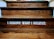 Wooden steps with a motivational quote displayed in bold white letters reading 'I BECOME WHAT I BELIEVE.' The texture of the wood grain is visible, and there is a dim lighting atmosphere.