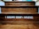 Wooden steps with a motivational quote displayed in bold white letters reading 'I BECOME WHAT I BELIEVE.' The texture of the wood grain is visible, and there is a dim lighting atmosphere.