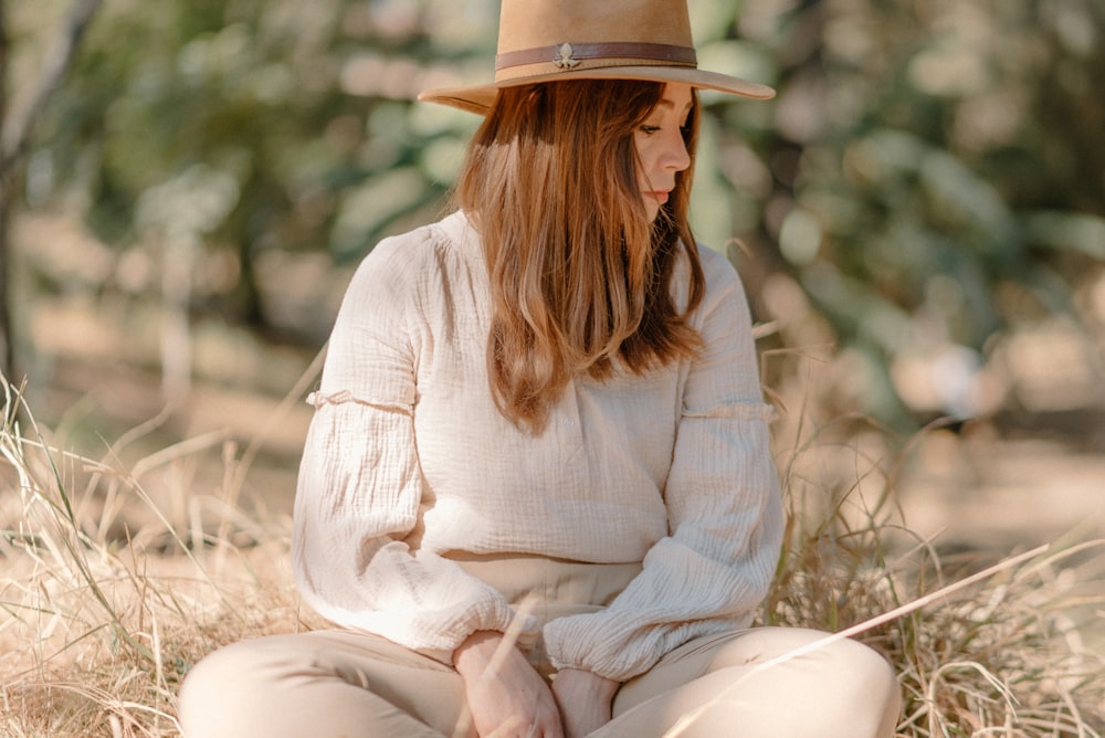 a woman sitting on the ground wearing a hat