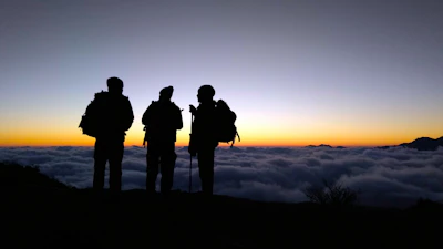 Silhouettes of hikers pausing on a cliff edge overlooking a vast ocean at sunset.
