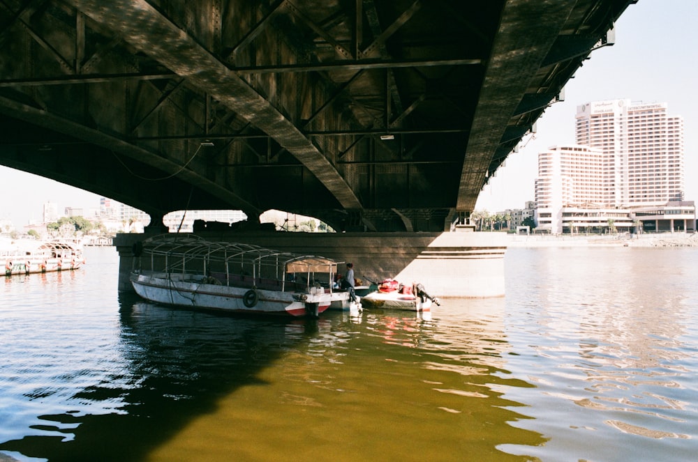 a boat floating under a bridge next to a body of water