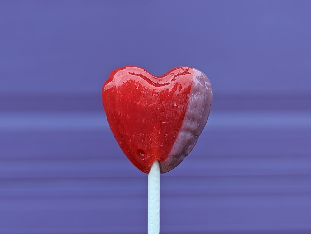 a heart shaped lollipop sitting on top of a white stick