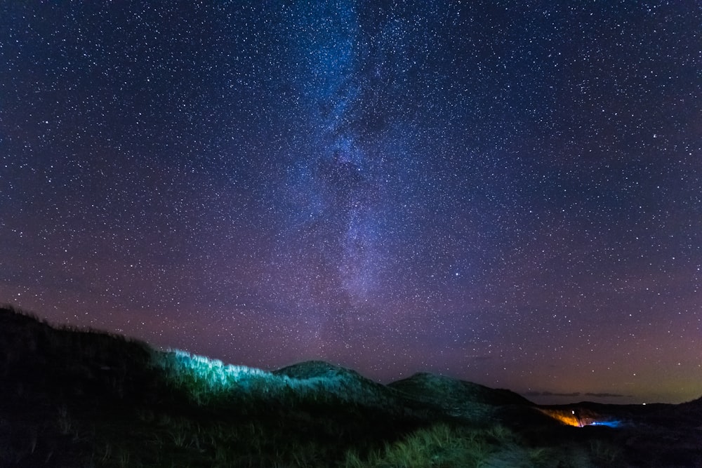 the night sky with stars above a grassy hill
