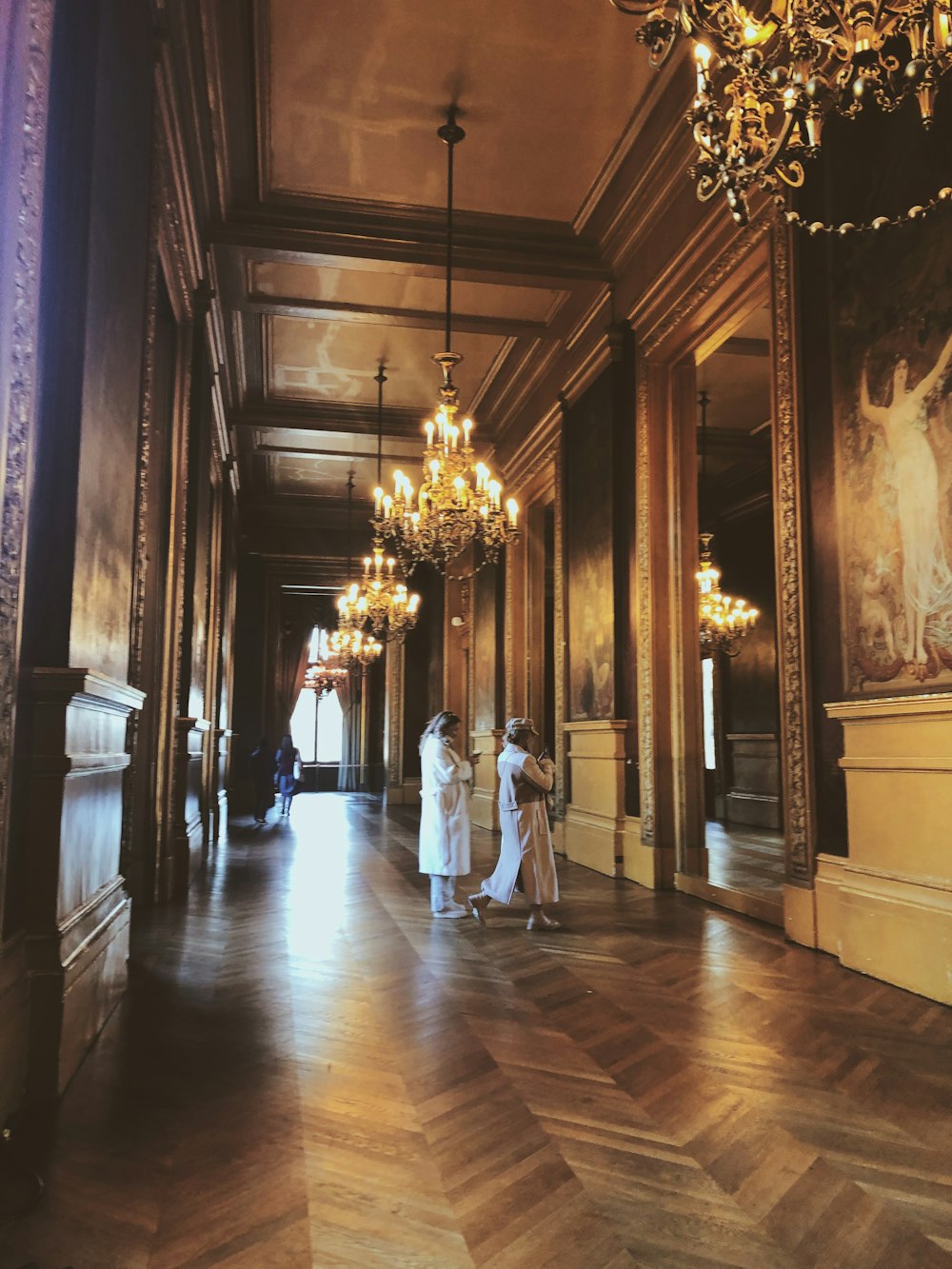 a couple of women standing in a hallway next to a chandelier