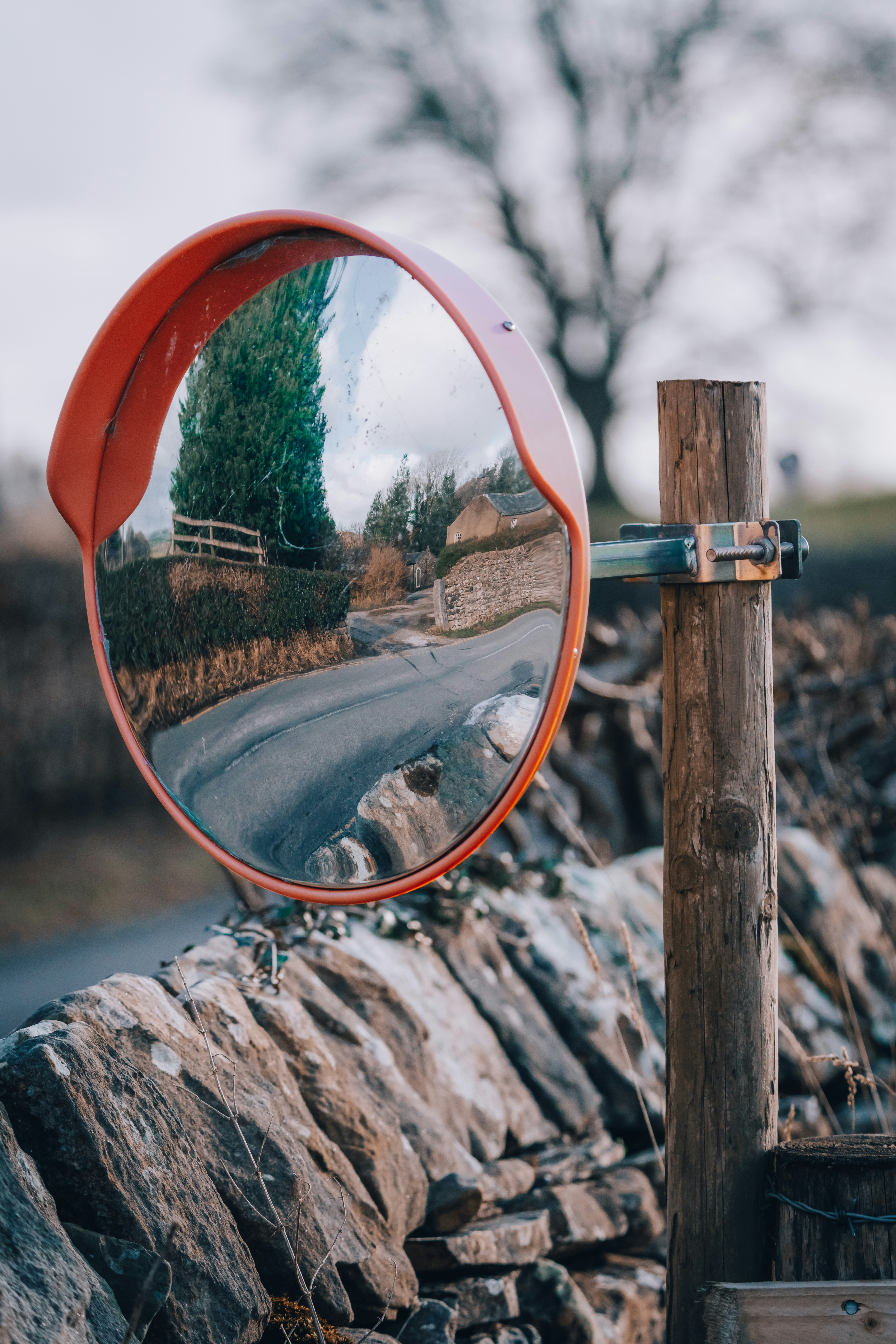 a red mirror on a wooden pole next to a road