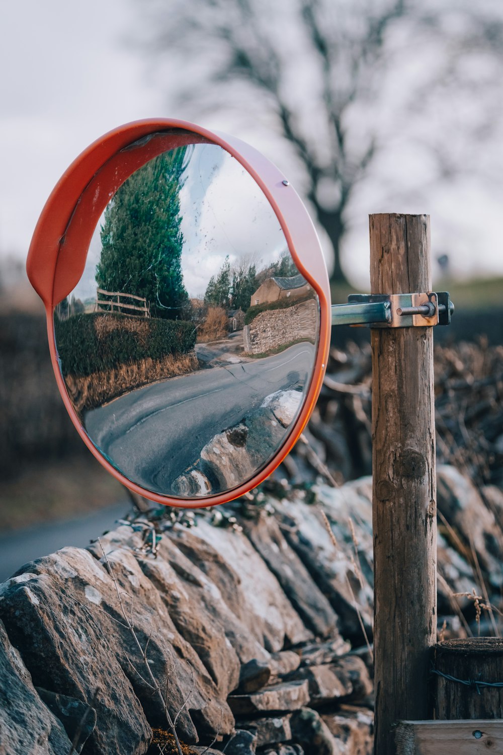 a red mirror on a wooden pole next to a road
