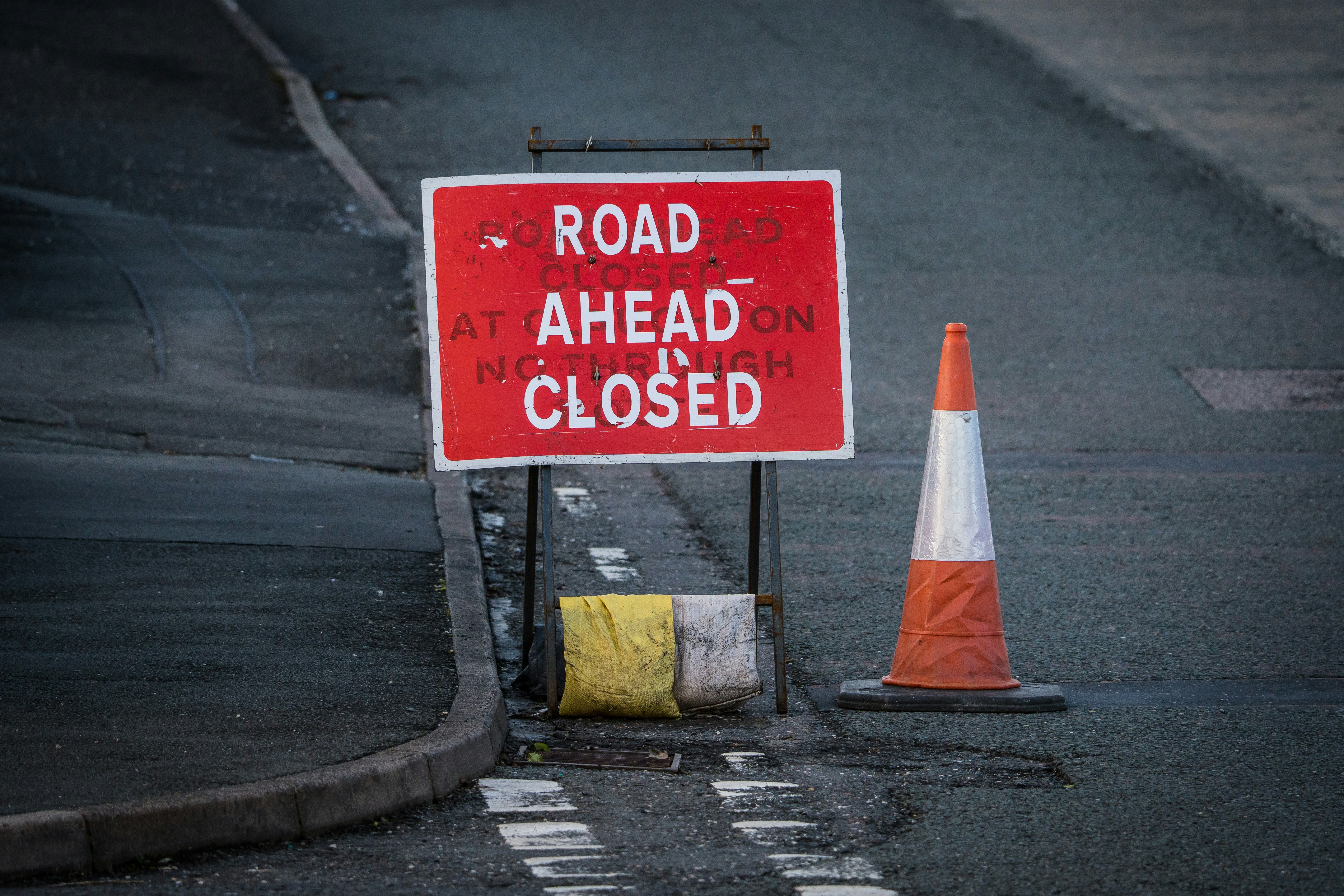 a road closed sign next to a traffic cone