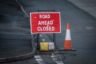 a road closed sign next to a traffic cone