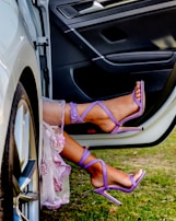 a woman's feet in purple shoes sitting on the door of a car