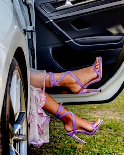 a woman's feet in purple shoes sitting on the door of a car