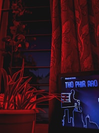 A sleek dark-themed TV studio with glowing red accent lights and a large video screen displaying a live news broadcast.