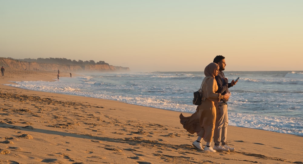 a man and woman standing on a beach next to the ocean