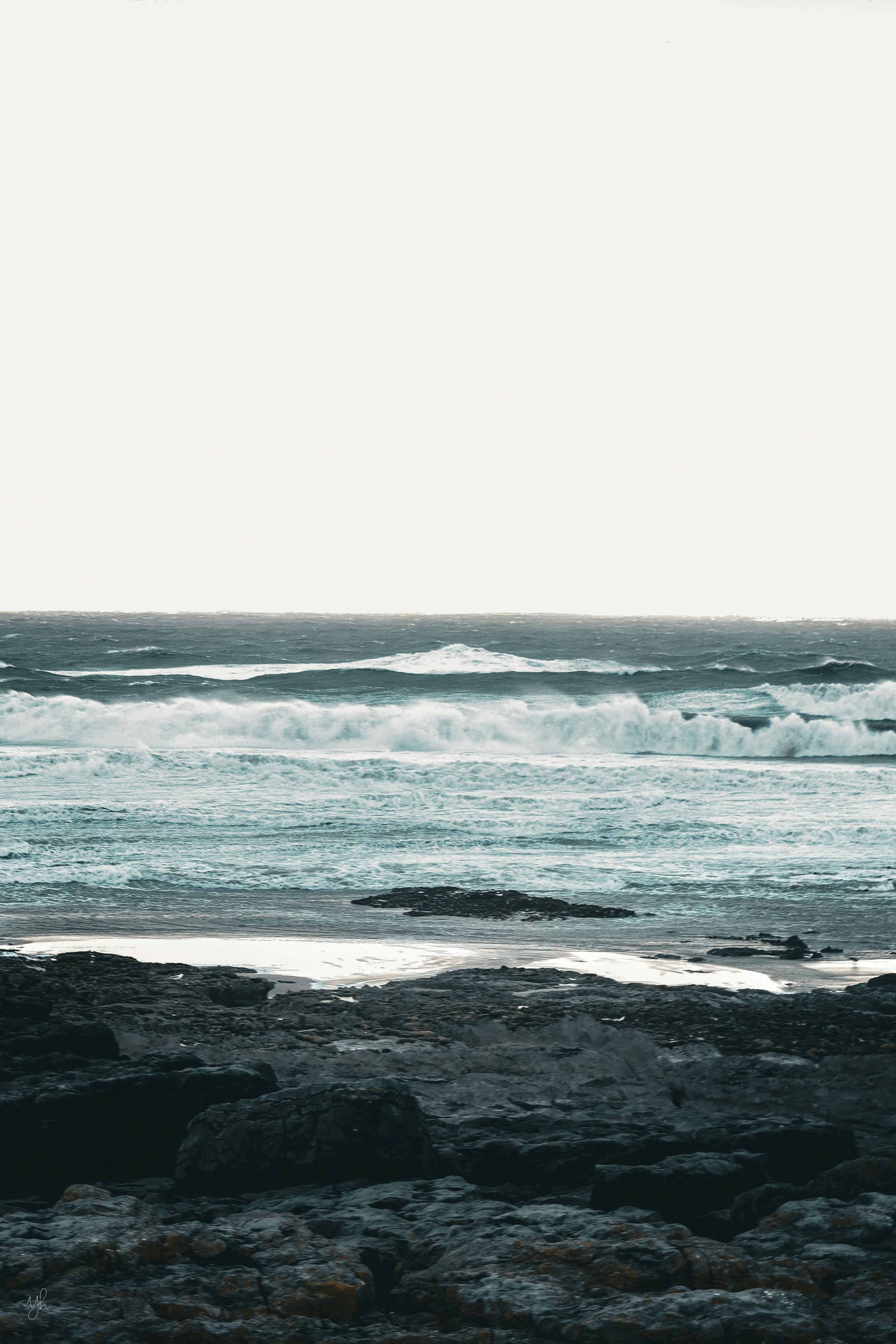 A person standing on a rocky beach holding a surfboard photo Free