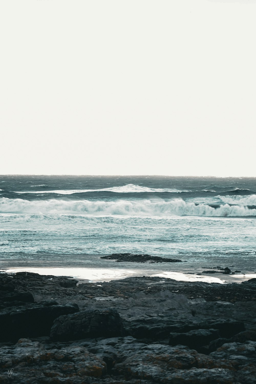 a person standing on a rocky beach holding a surfboard