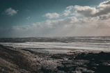 Coastline with crashing waves against jagged cliffs under a moody, overcast sky.