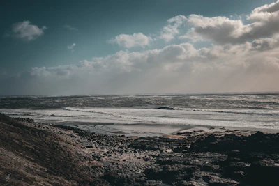 A dramatic sky over a rugged coastline, clouds swirling above crashing waves.