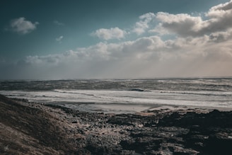 The rugged coastline of Galicia under a dramatic cloudy sky, waves crashing against cliffs.