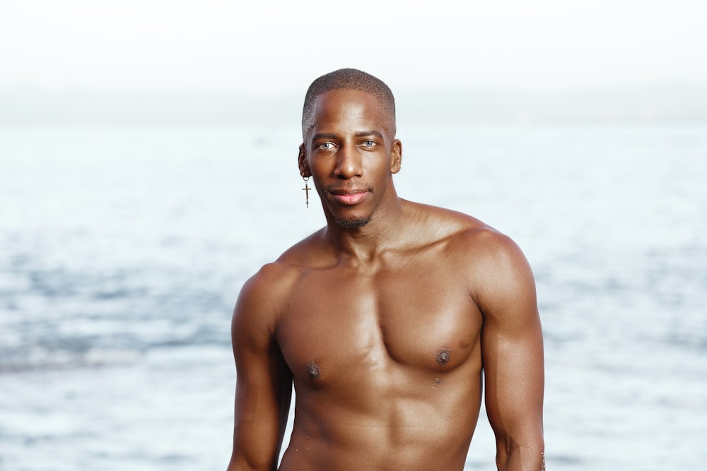 a man without a shirt standing in front of the ocean