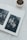 A photo album opened to a page displaying two black and white photographs. The left photo features a man standing by a tree, and the right photo shows a couple dancing under string lights. A small potted succulent is placed next to the album on a soft, white surface.