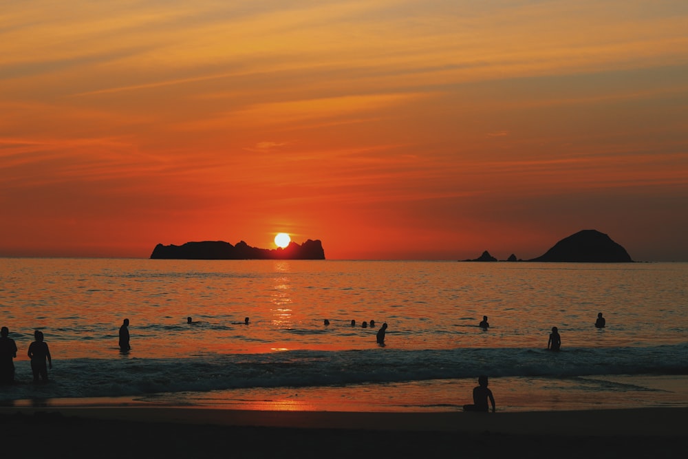 a group of people standing on top of a beach at sunset