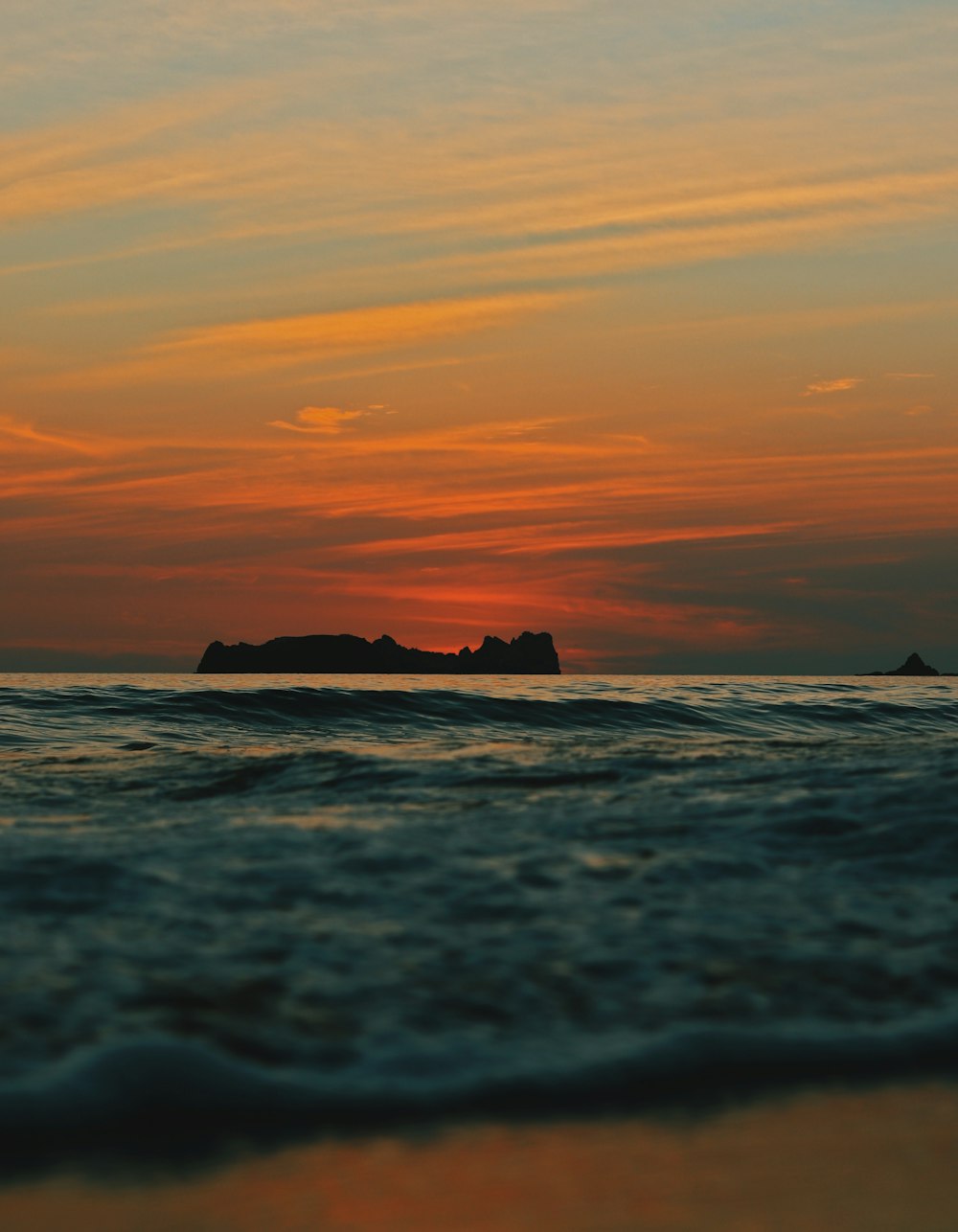 a sunset over the ocean with a small island in the distance