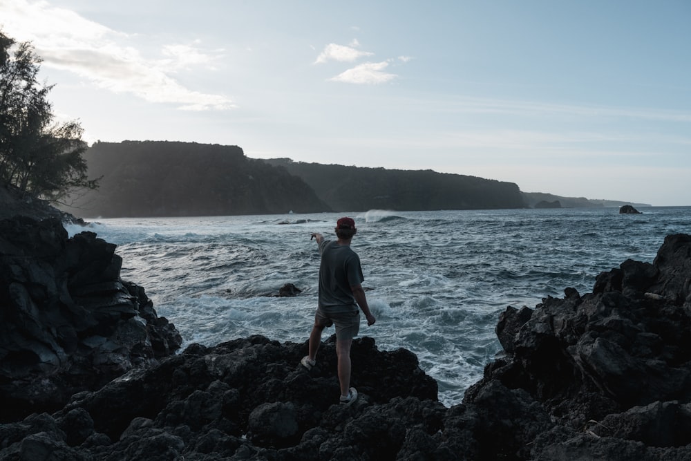 a man standing on top of a rocky beach next to the ocean