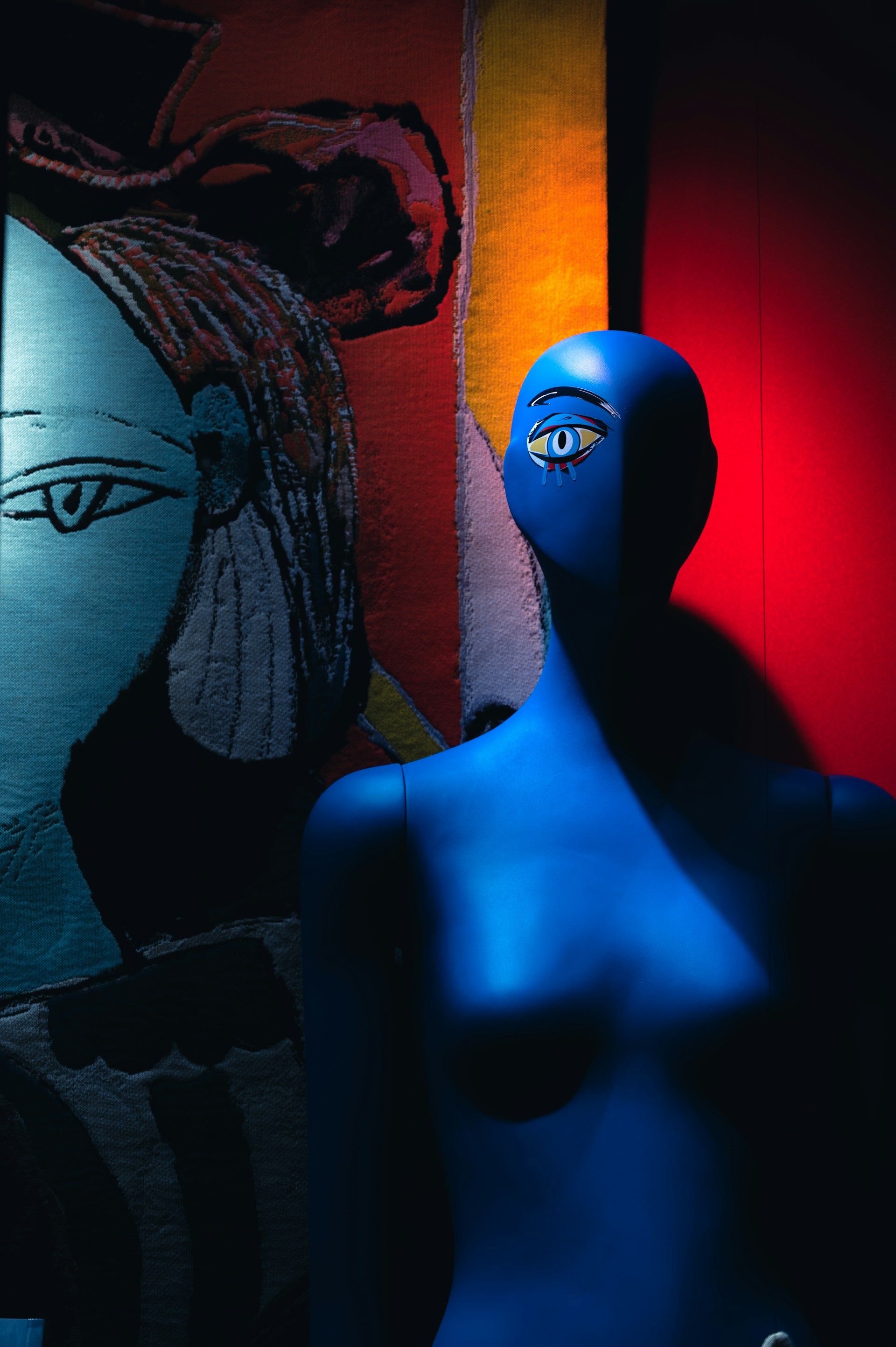 a blue mannequin standing in front of a painting