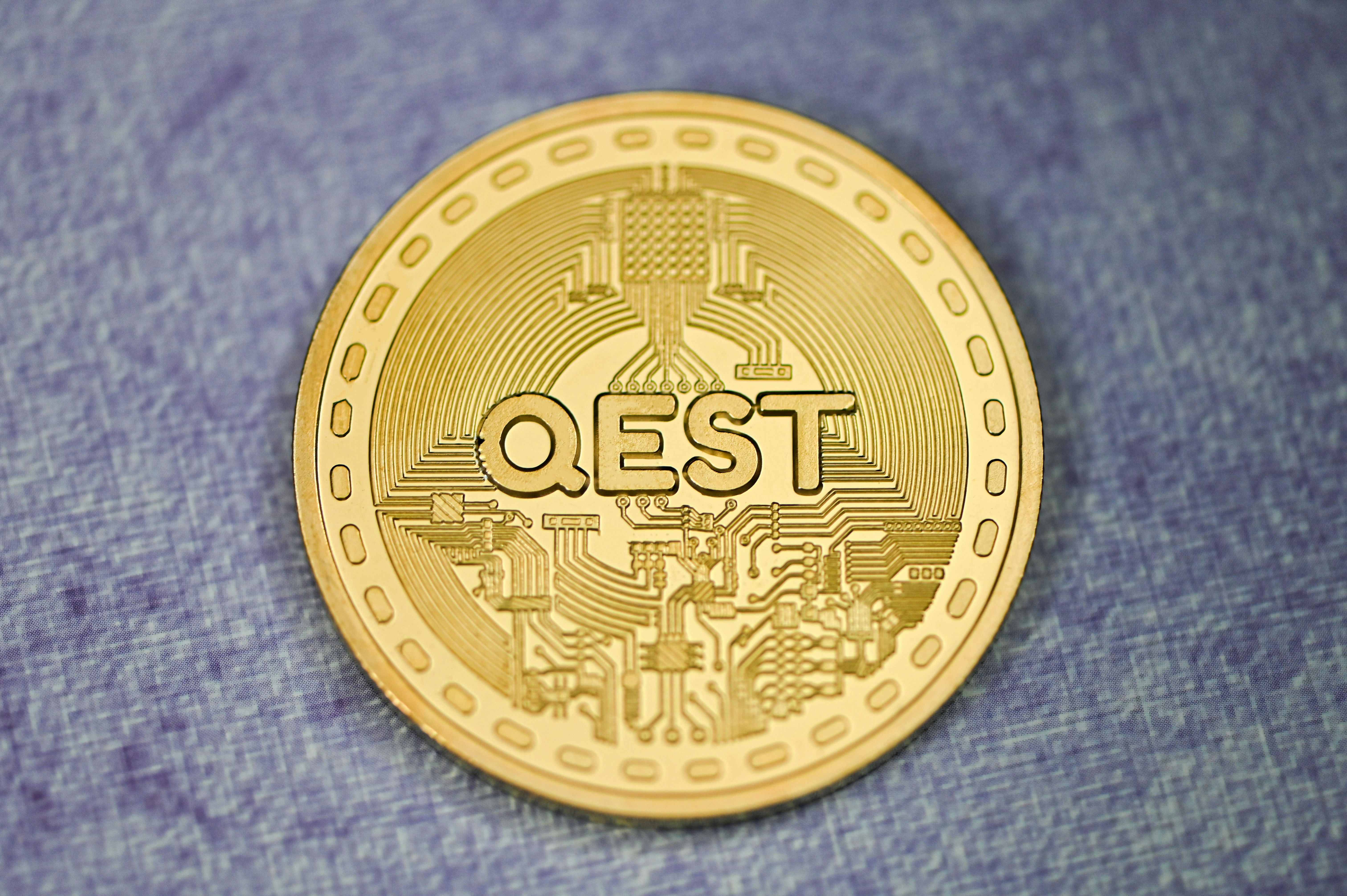 A gold QEST coin on a blue background