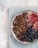 A bowl filled with a mix of cereal clusters, blueberries, and slices of blood orange placed on a textured blue napkin. The bowl is set against a light, neutral-toned background, creating a fresh and inviting composition.