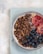 A bowl filled with a mix of cereal clusters, blueberries, and slices of blood orange placed on a textured blue napkin. The bowl is set against a light, neutral-toned background, creating a fresh and inviting composition.
