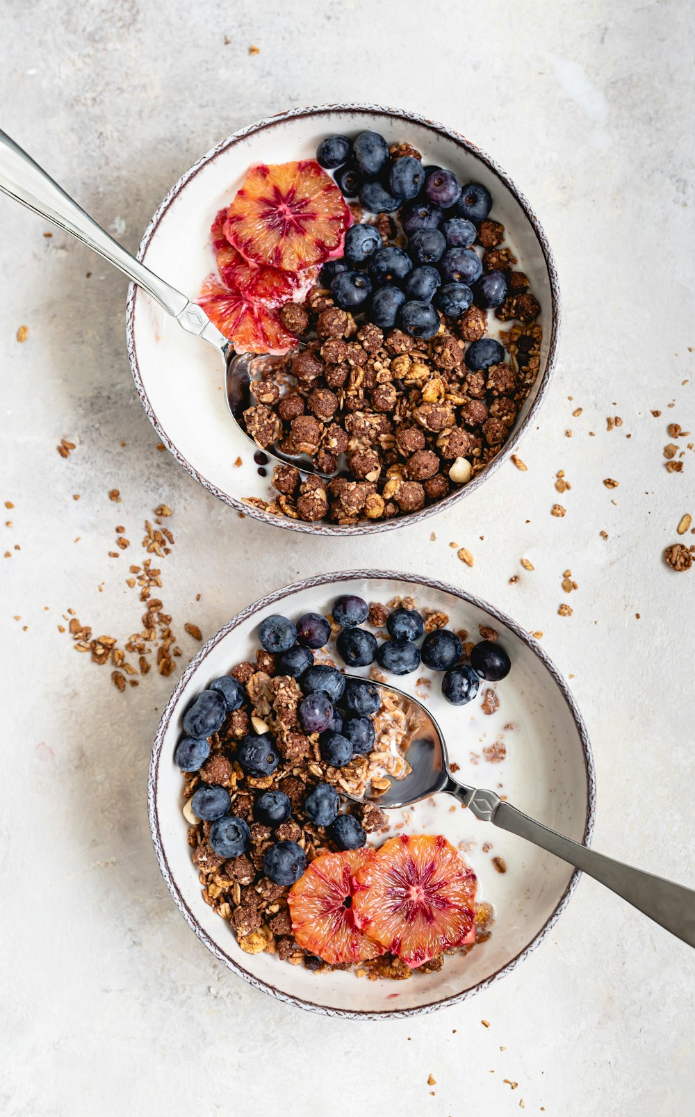 two bowls filled with granola and fruit on top of a table