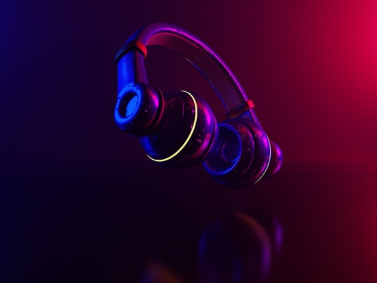 Floating headphones illuminated by a dynamic mix of neon purple, pink, and blue lighting, creating a futuristic and sleek appearance. The reflective surface of the headphones adds to the modern aesthetic, emphasizing the contours and form of the device.