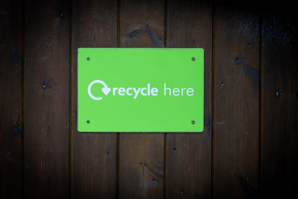 a green recycle here sign on a wooden wall