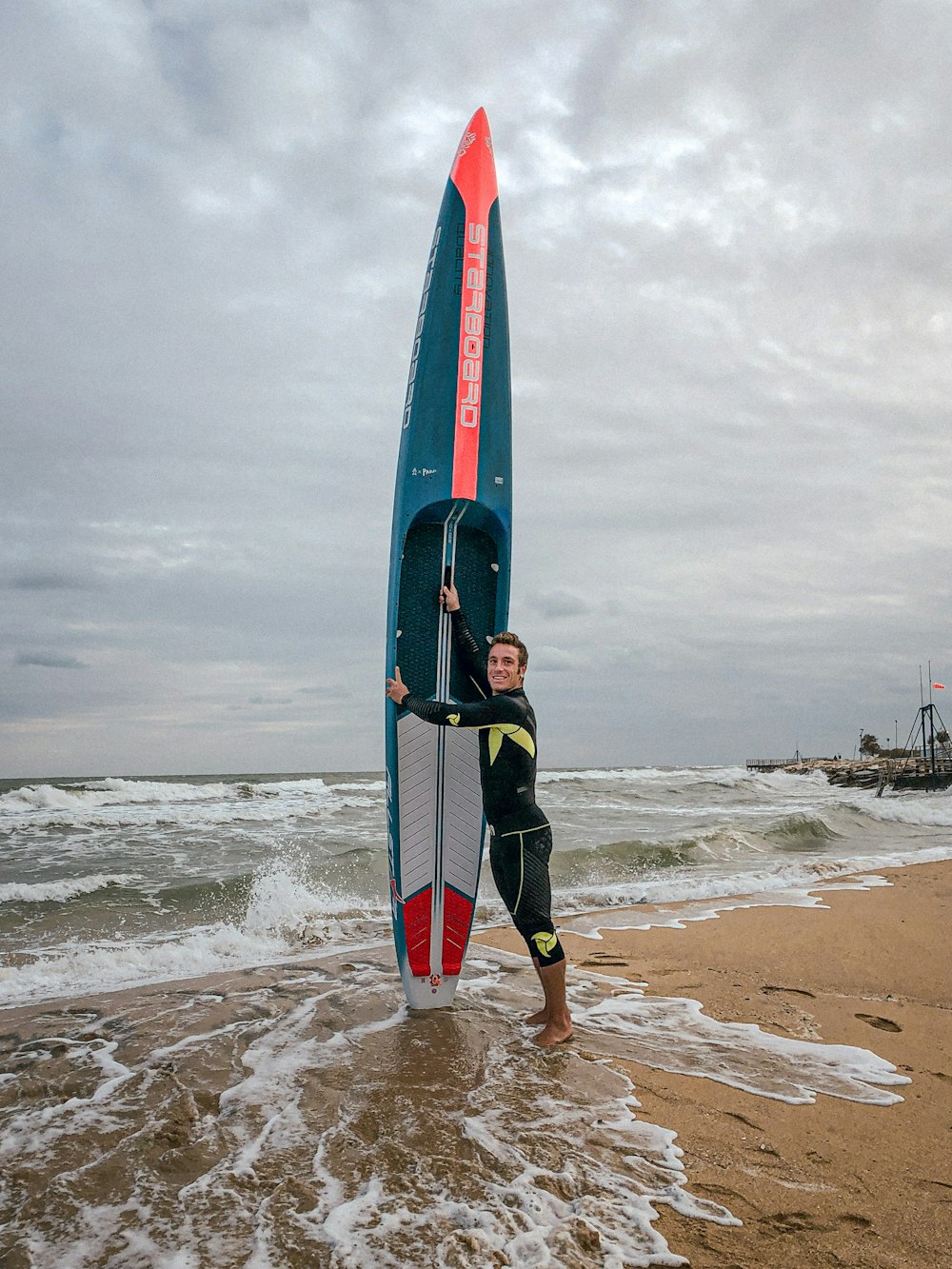 Un uomo che tiene una tavola da surf in cima a una spiaggia sabbiosa