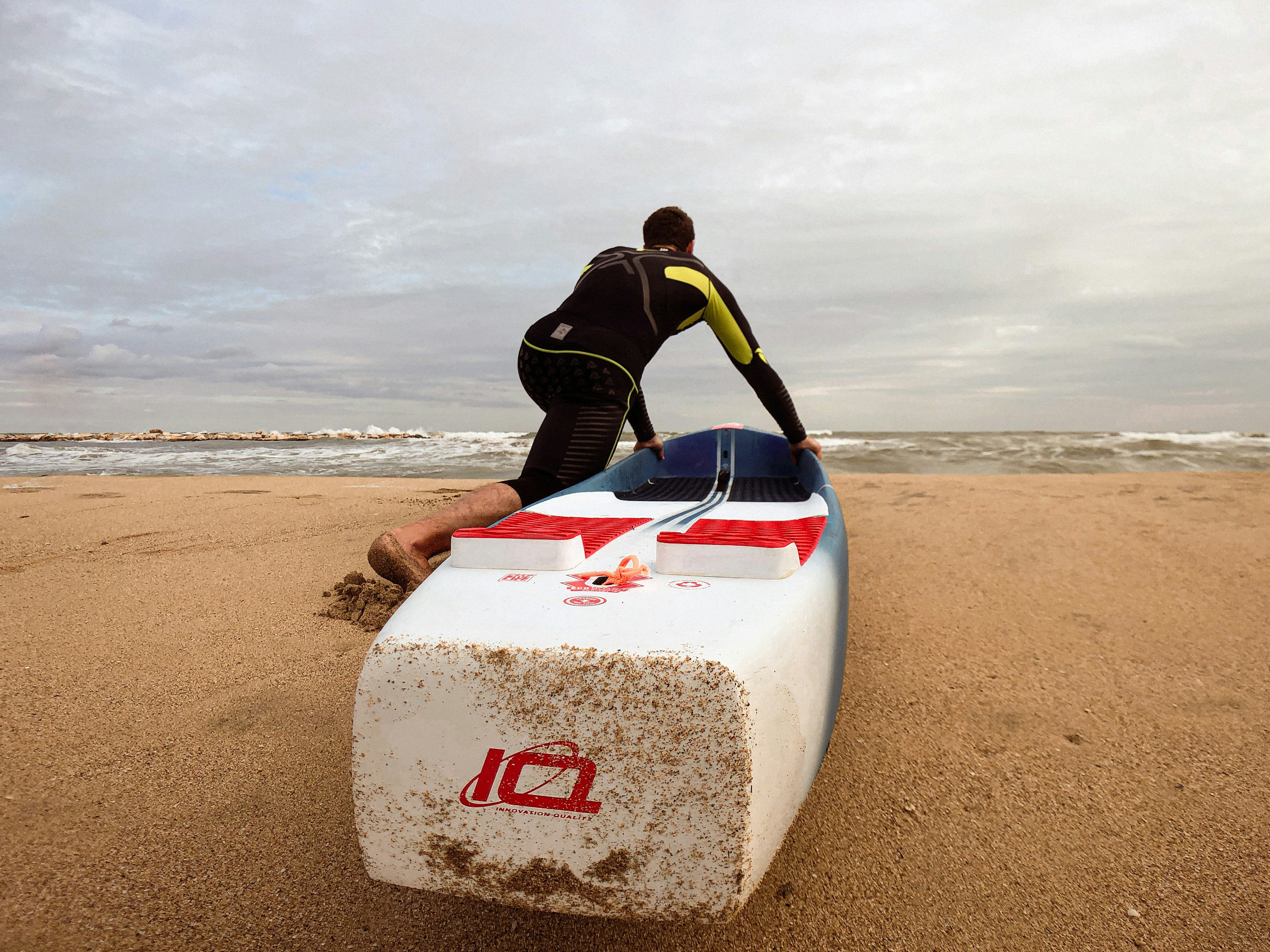 a man in a wet suit standing next to a surfboard on the beach
