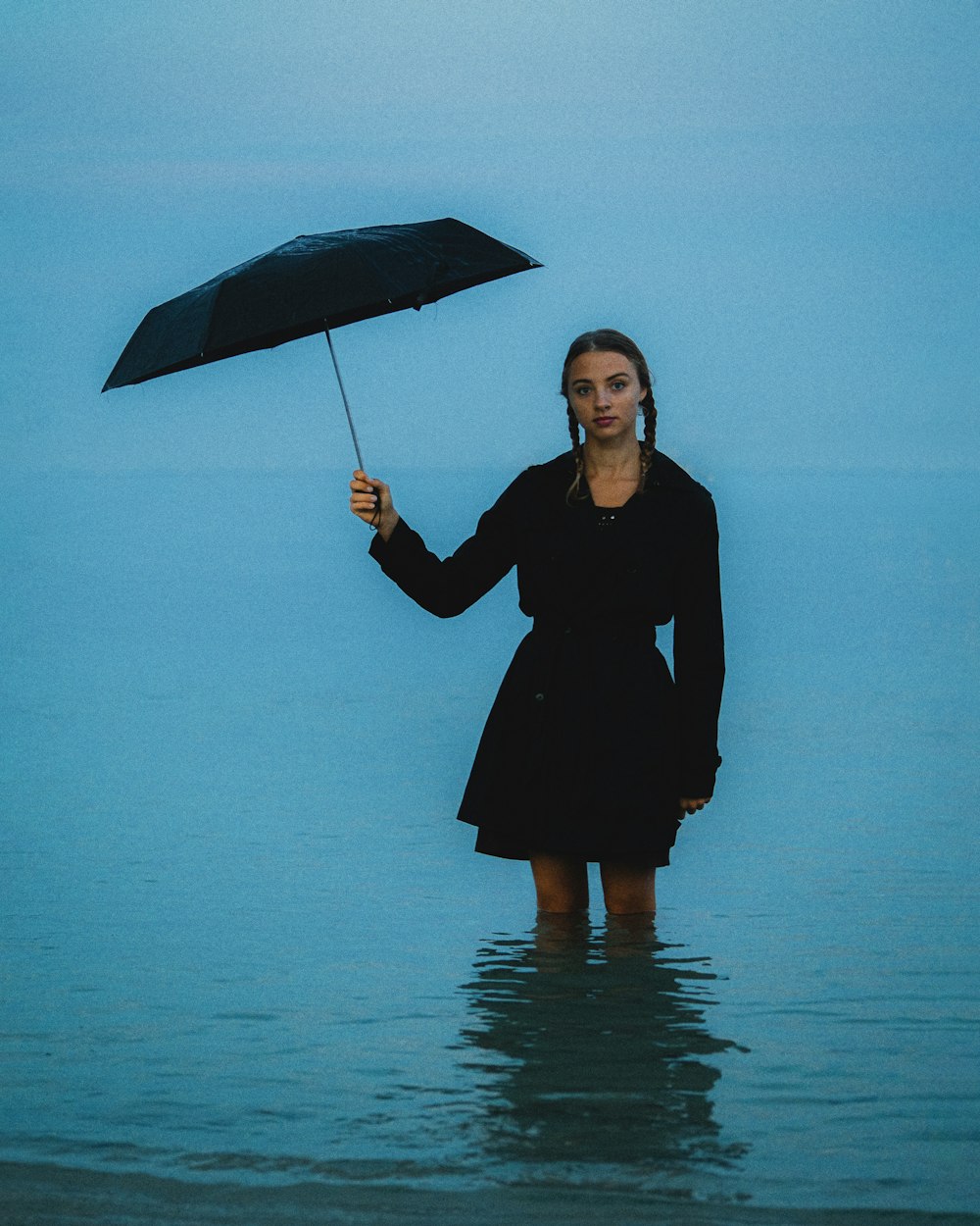 a woman standing in the water holding an umbrella