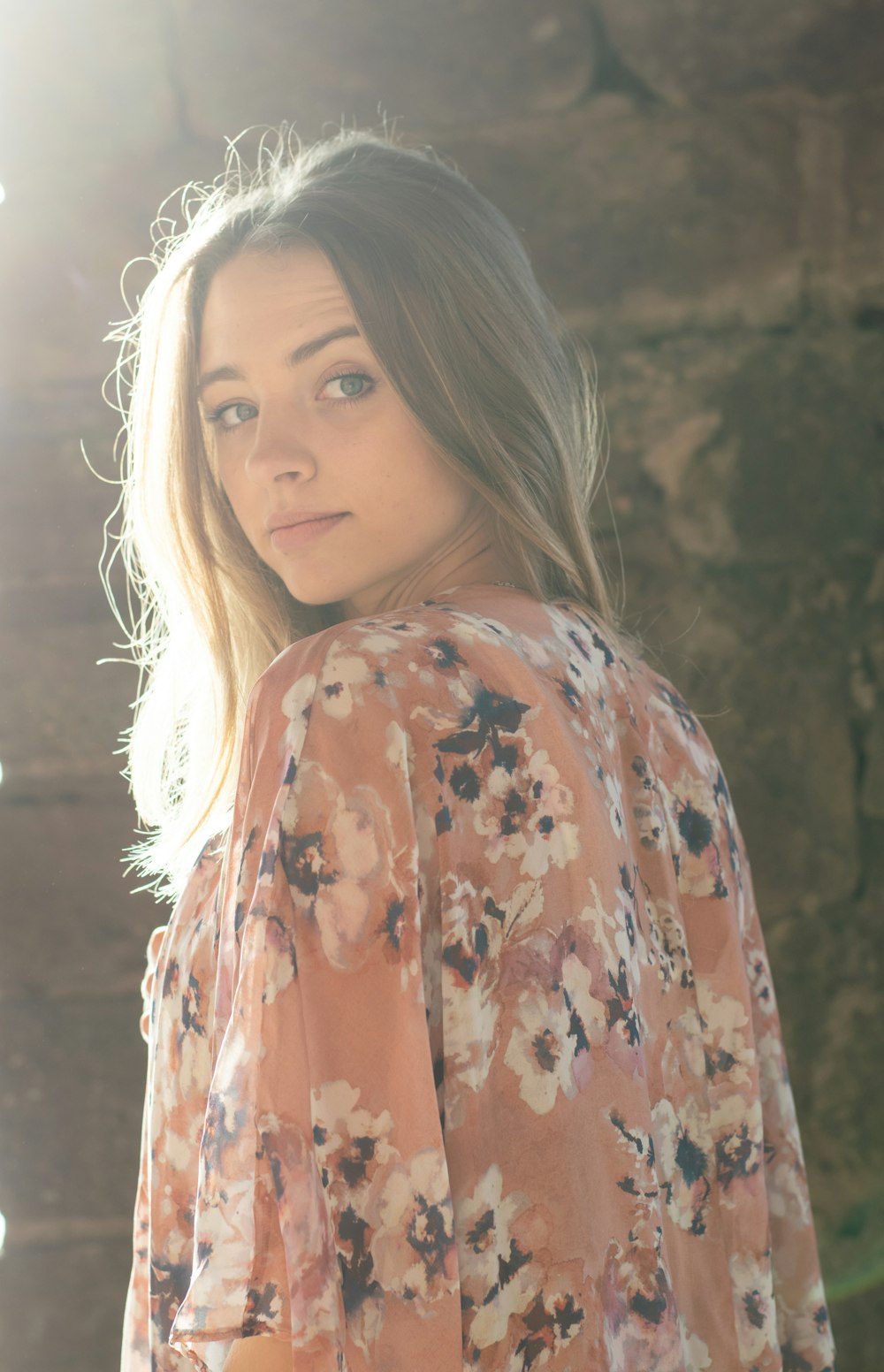 a beautiful young woman standing in front of a stone wall