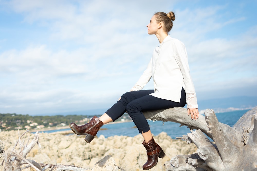 a woman sitting on top of a tree branch next to the ocean