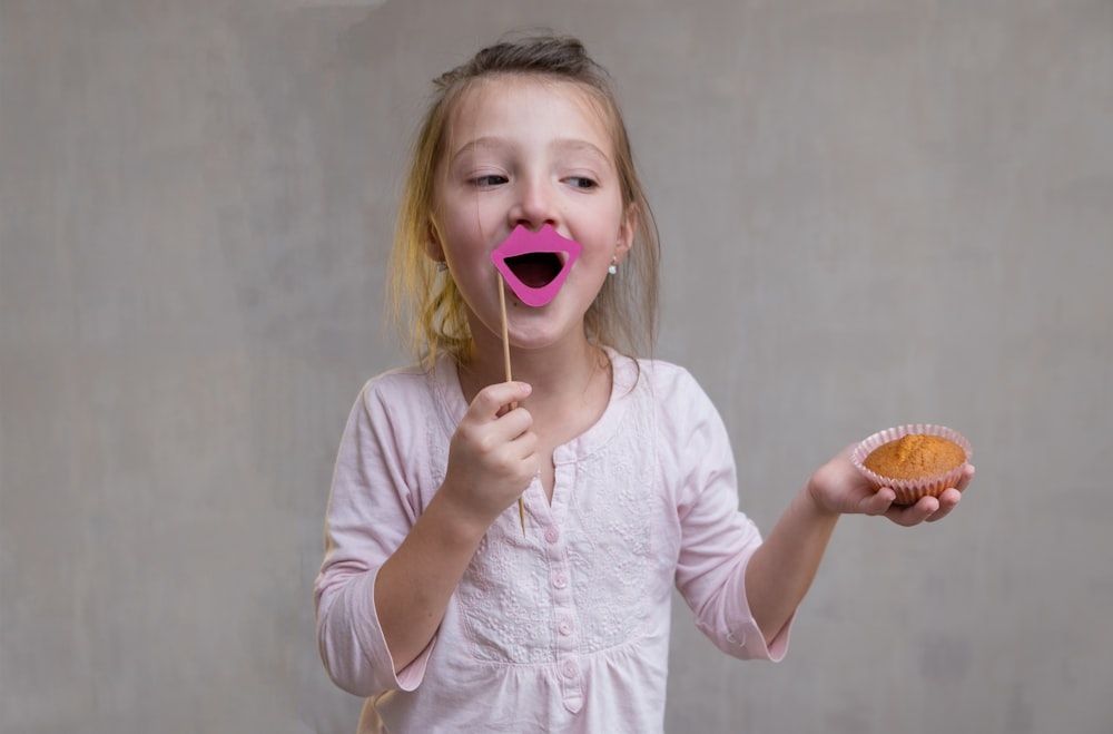 a little girl holding a donut and sticking a pink tongue out