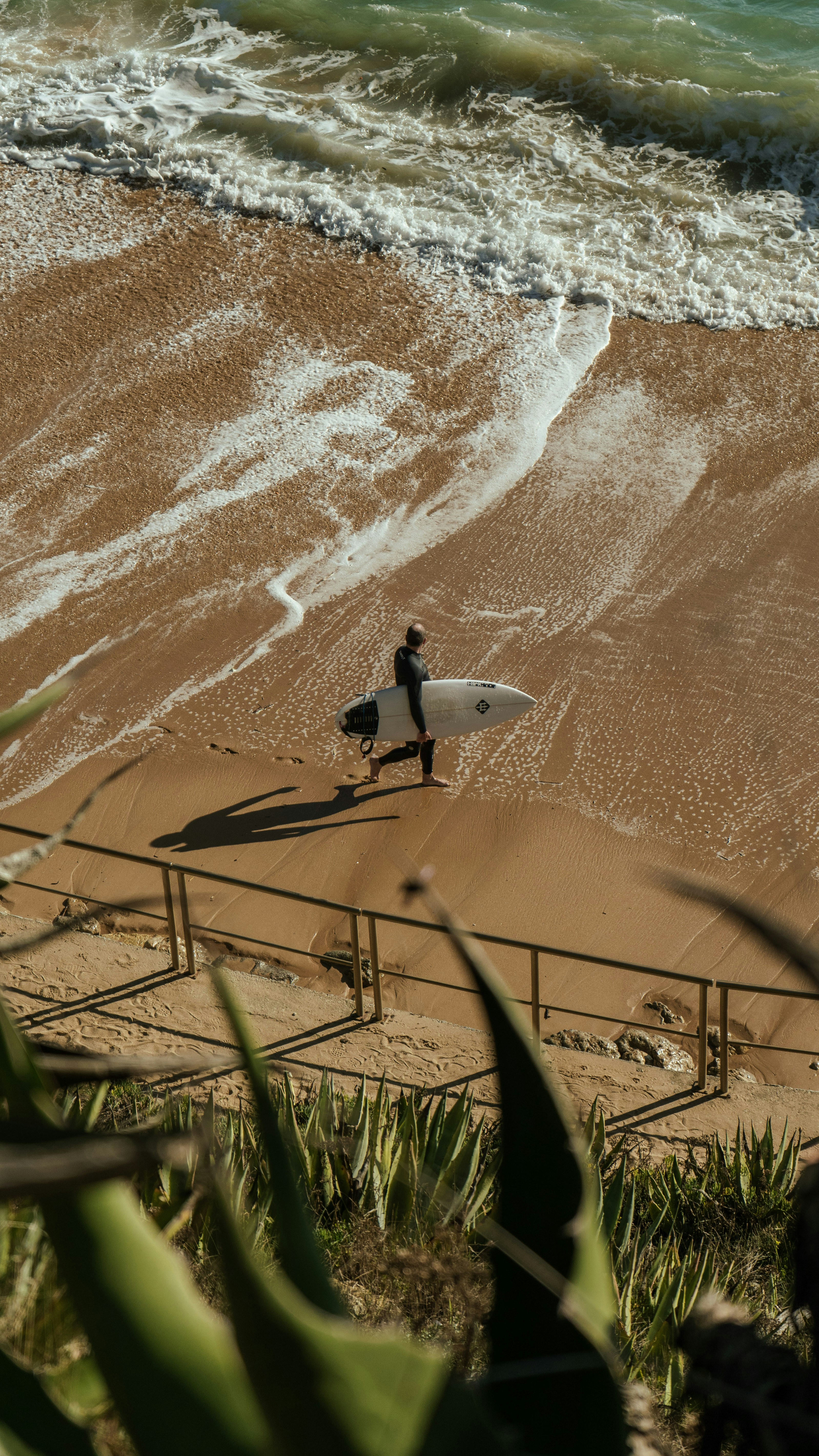 a man carrying a surfboard on top of a sandy beach