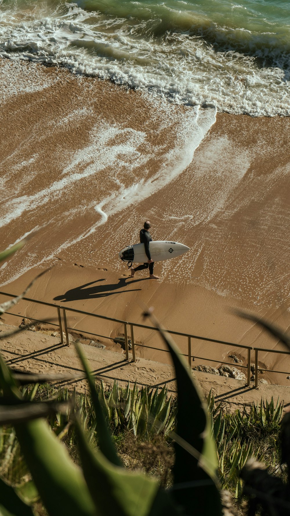a man carrying a surfboard on top of a sandy beach