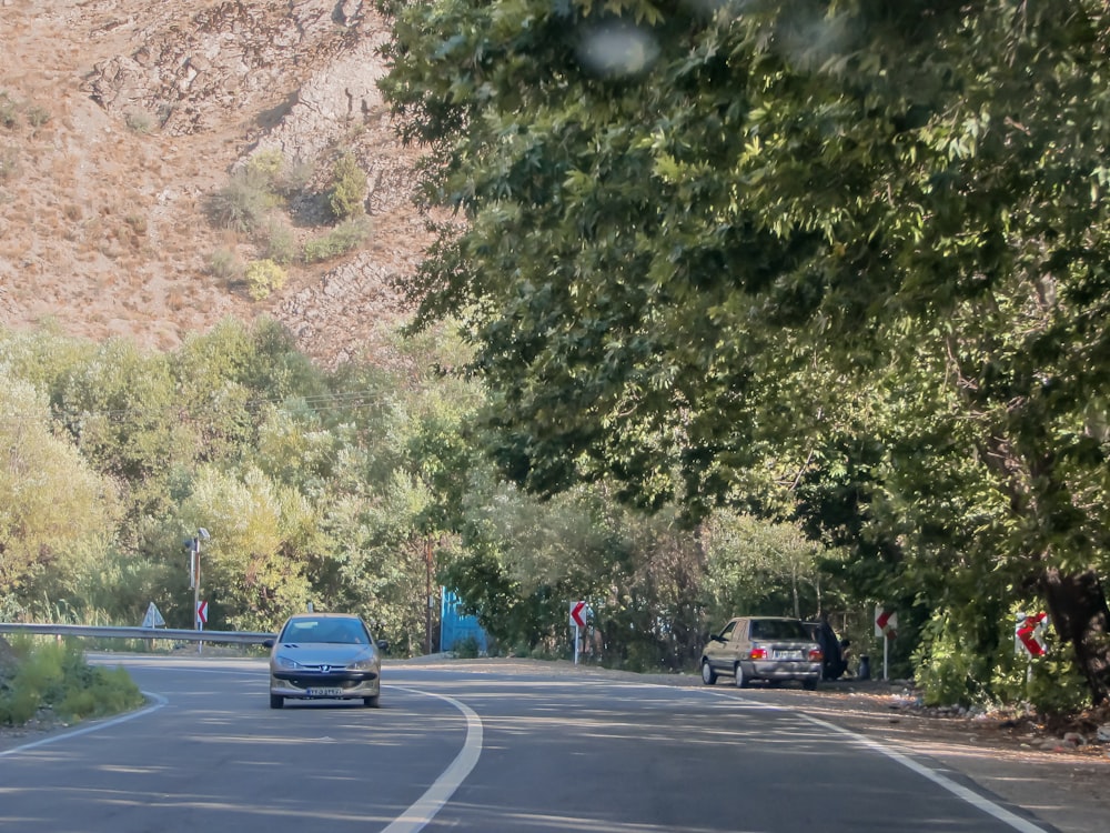 a car driving down a road next to a lush green hillside