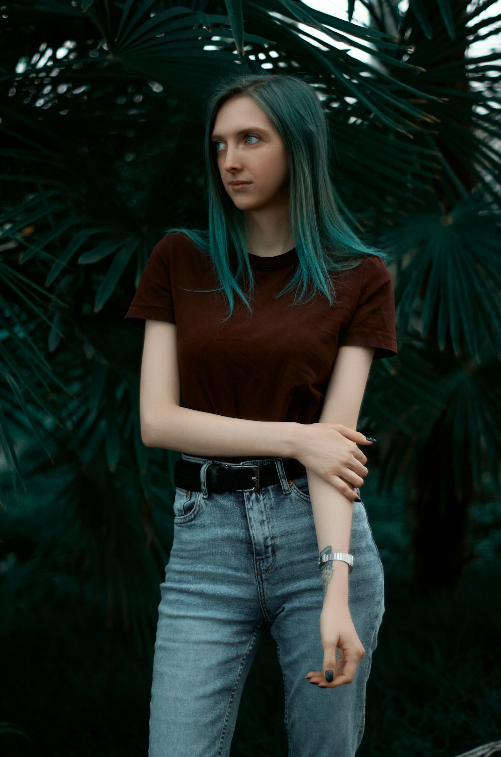 a woman with blue hair standing in front of a palm tree