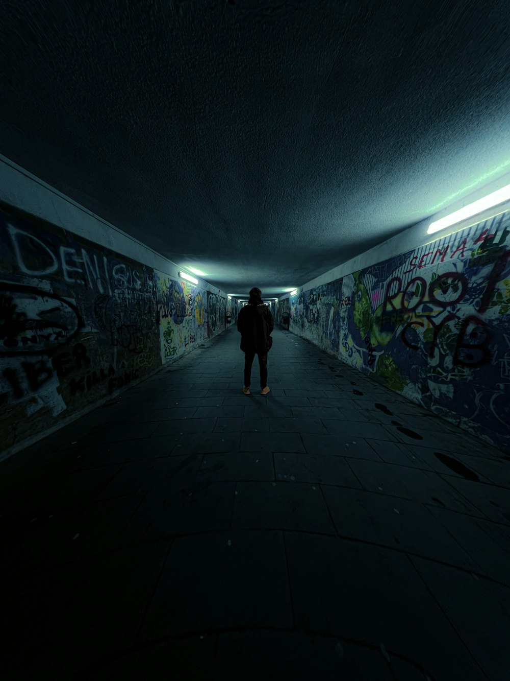 a man walking down a dark tunnel covered in graffiti