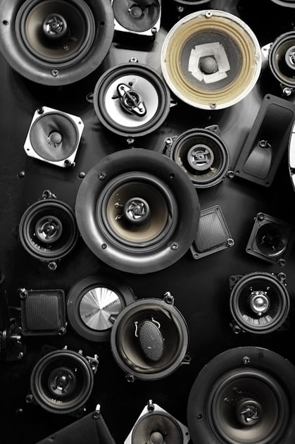 Multiple car audio speakers of different sizes laid out on a dark surface showing various driver types and impedance configurations