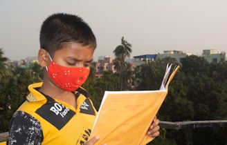 a young boy wearing a face mask and reading a book