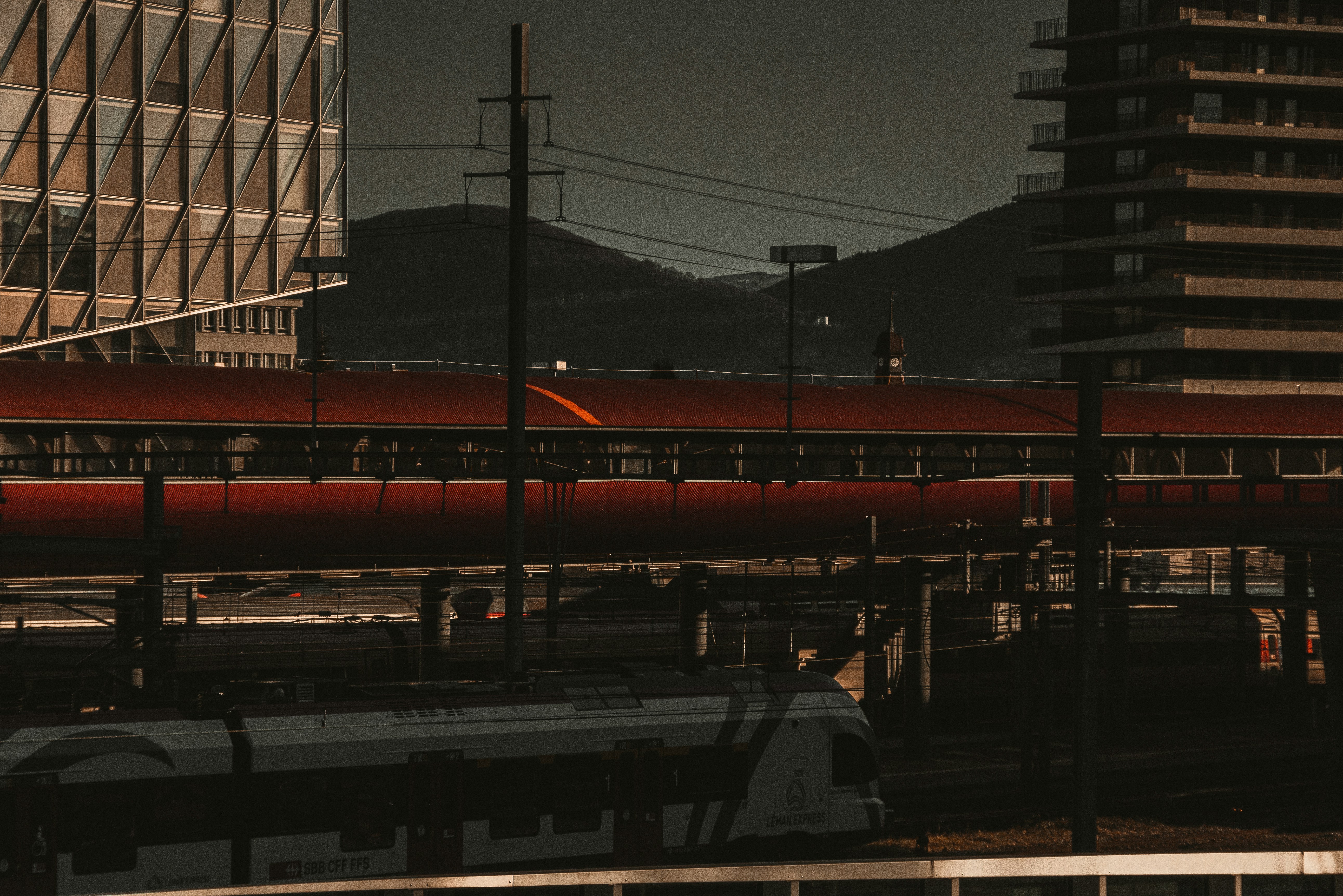 a red train traveling down train tracks next to tall buildings, 