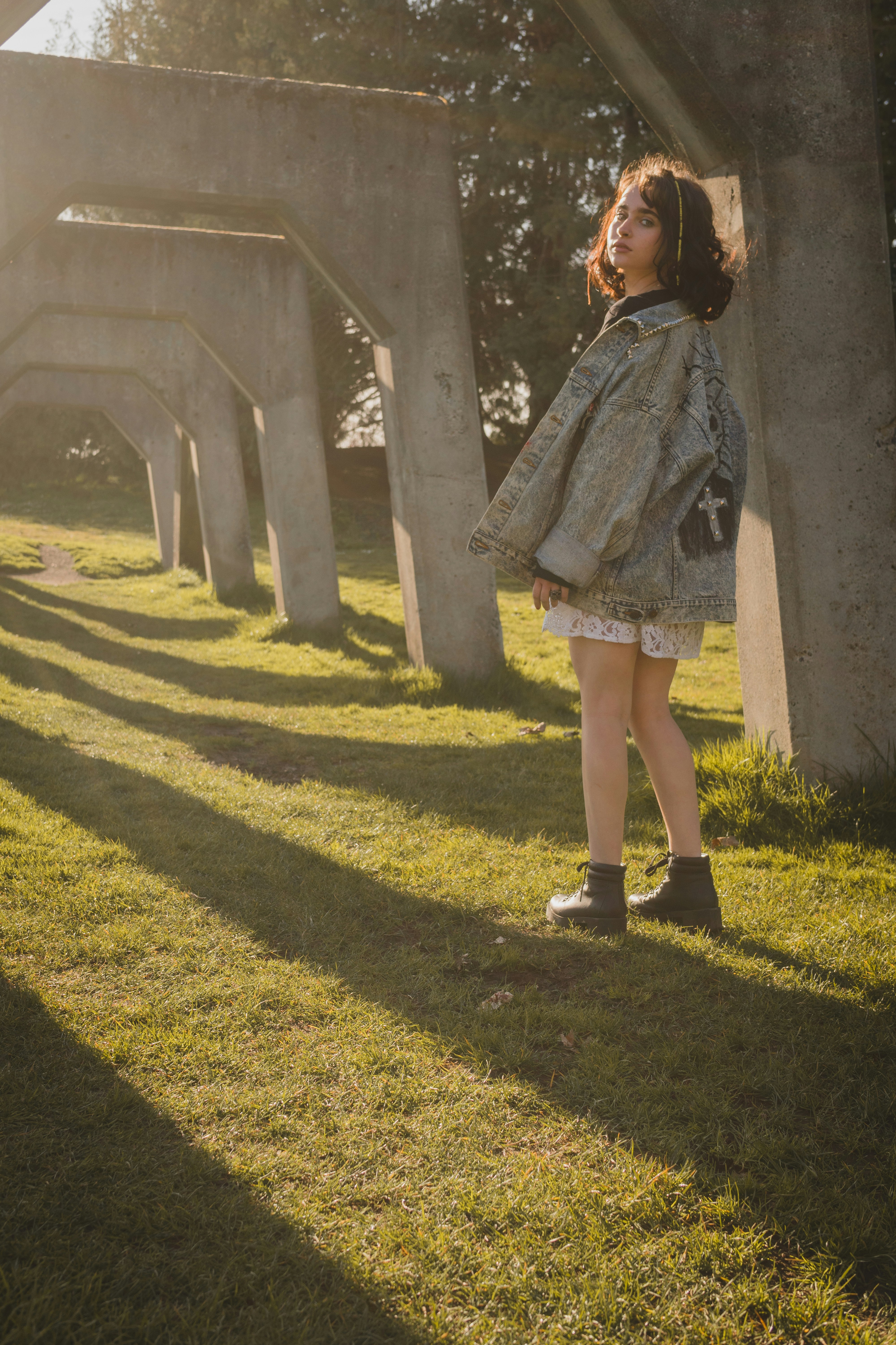 a little girl standing in the grass under a bridge