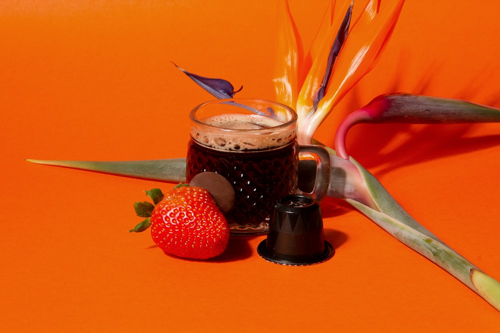 a cup of coffee next to a strawberry on an orange background